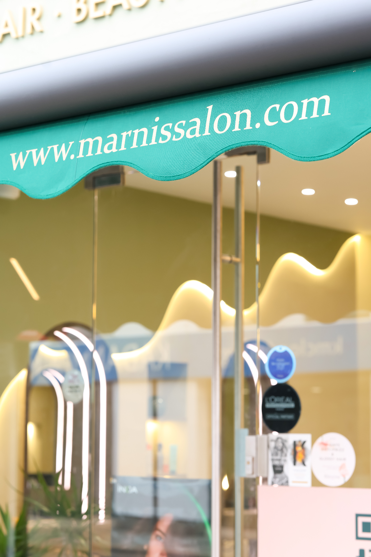 Marnis signature scalloped teal awning with marnissalon.com wordmark above the glass shopfront